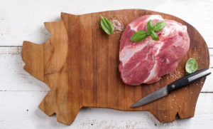 raw pork slab on a pig shaped cutting board with knife
