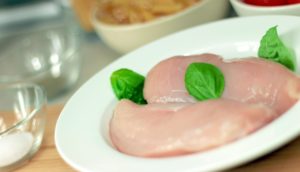 closeup of raw turkey hen breast on a plate with ingredients visible around it
